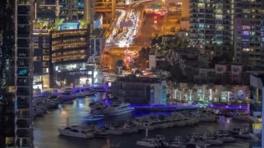 Limanda gece vakti yüzen yatların hava görüntüsü. Dubai Marina 'da limana yakın park edilmiş beyaz tekneler var. Bir yol kavşağında trafik