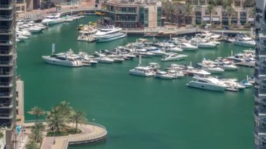 Limanda yüzen yatların hava görüntüsü zaman ayarlı. Dubai Marina 'da limana yakın park edilmiş beyaz tekneler var. Avuç içleriyle gezinme