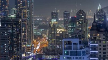 Dubai Marina ve Medya Şehri bölgelerinde modern gökdelenler ve ofis binaları gece uçuşları. Üst geçitte trafik ve şehir merkezindeki kulelerde kavşak.
