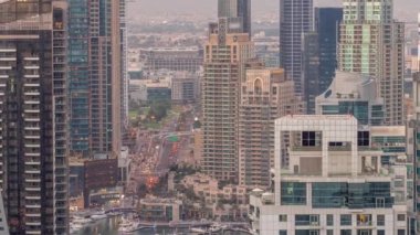 Dubai Marina ve Medya Şehri 'nin modern gökdelenleri ve ofis binaları ile hava gününden geceye geçiş zamanı. Yeşil park yakınlarındaki üst geçitte trafik ve kavşak.
