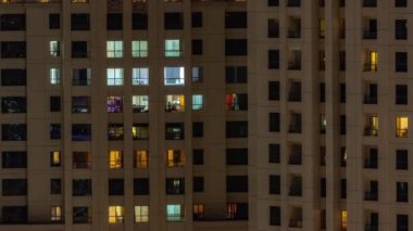 Oturma odalarında parlayan pencereleri olan bir apartman dairesinin akşam manzarası. Işıklı gökdelenle aydınlatılmış yüksek bir gökdelen