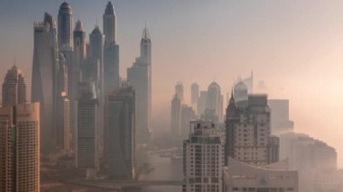 Sunrise Airial Timelapse sırasında Dubai Marina 'nın en yüksek karşılama bloğundaki yapay kanallı çeşitli gökdelenlerin görüntüsü. Birçok kule ve yat sabah sisi ile kaplandı.