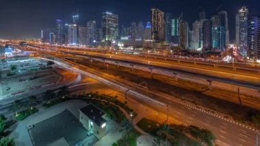 Dubai Marina gökdelenleri ve Şeyh Zayed yolu ile metro demiryolu gece panoramik zaman çizelgesi. Modern kulelerin yakınındaki bir otoyolda trafik var, Birleşik Arap Emirlikleri