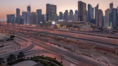 Dubai Marina gökdelenleri ve Şeyh Zayed yolu ile metro demiryolu havadan geceye geçiş panoramik zaman çizelgesi. Günbatımından sonra modern kulelerin yakınındaki bir otoyolda trafik, Birleşik Arap Emirlikleri