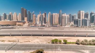 Dubai Marina gökdelenleri ve Şeyh Zayed yolu ile metro demiryolu zaman çizelgesine sahip Panorama. Modern kulelerin yakınındaki bir otoyolda trafik var, Birleşik Arap Emirlikleri