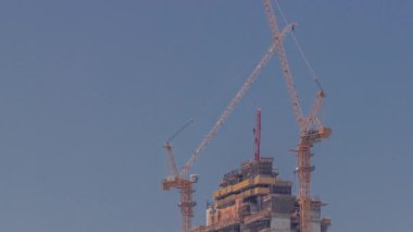 Vinçlerin zaman ayarlı olduğu gökdelen yapım aşamasında. Çok katlı yeni bir kule inşaatı. İnşaatçılar tepede çalışıyor.