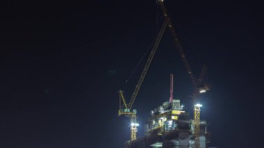 Gökdelen yapım aşamasında ve vinçler gece zaman ayarlı. Çok katlı yeni bir kule inşaatı. İnşaatçılar tepede çalışıyor.