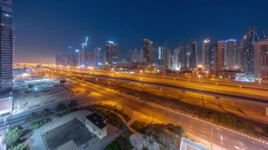 Dubai Marina gökdelenleri ve Şeyh Zayed yolu ile gece gündüz metro havası geçiş panoramik zaman çizelgesi. Gündoğumundan önce modern kulelerin yakınındaki bir otoyolda trafik vardı, Birleşik Arap Emirlikleri