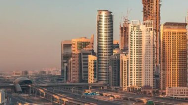 Dubai Marina 'da gökdelenler üzerinde uzun gölgeler ve gün doğumunda metro raylı Şeyh Zayed yolu. Modern kulelerin yakınındaki bir otoyolda trafik var, Birleşik Arap Emirlikleri