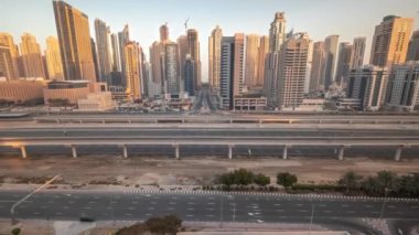 Dubai Marina gökdelenleri ve Şeyh Zayed yolu ile metro demiryolu sabah saatleri. Gündoğumu sırasında modern kulelerin yakınındaki bir otoyol trafiğine tepeden bakan panoramik, Birleşik Arap Emirlikleri