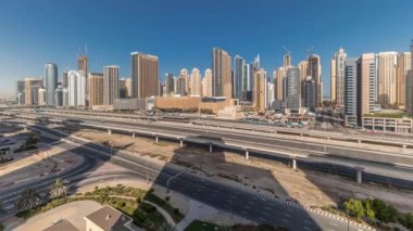 Panorama, Dubai Marina gökdelenlerini ve Şeyh Zayed yolunu metro demiryolu zaman çizelgesiyle gösteriyor. Modern kulelerin yakınındaki bir otoyolda trafik var, Birleşik Arap Emirlikleri