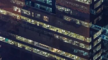 Yüksek katlı ofis binasının pencereleri gecenin geç saatlerinde parlayan ve yanıp sönen iç ışıkları olan dış kısımda. Havadan üst görünüm