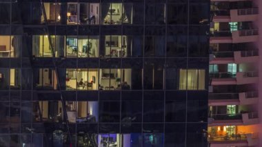 Modern ofisteki pencere ışıkları ve gece vakti balkonlu binalar. İçinde aydınlık odalar olan çok katlı gökdelenler.