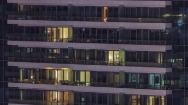 Geceleri modern binalardaki pencere ışıkları zaman ayarlı. İçinde aydınlık odalar olan çok katlı gökdelenler.