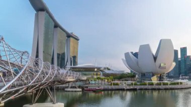 View of The Helix Bridge in Singapore day to night transition timelapse with illuminated skyscrapers on background. Pedestrian bridge linking Marina Centre with Marina South in the Marina Bay area in