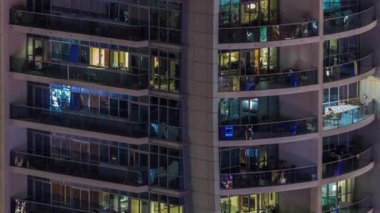 Dışarıdaki apartmanın gece manzarası renkli zaman çizelgesi. Pencerelerinde parlayan ışıklar olan yüksek katlı bir gökdelen. Işıklar cam yüzeyden yansıyor