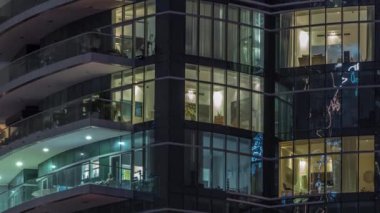 Pencerelerde çok katlı binaların panjurları ve havadan zaman ayarlı düz gece panoraması. Büyük bir şehirde aydınlık bir gökdelen.