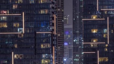 Çok katlı binaların pencerelerinde yanıp sönen çok renkli ışıklardan oluşan düz bir panorama. Büyük bir şehirde aydınlık bir gökdelen.