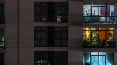 Gece saatlerinde apartmanın pencereleri, balkonunda sandalyeleri olan aydınlık evlerin ışıkları. Gökdelenlerin kentsel manzarası