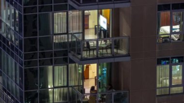 Apartman binasındaki parlayan panoramik pencerelerin gece görüşü. Odalarında ışıklar olan yüksek gökdelenli.