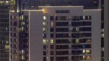 Pencereler, modern konut binalarında geceleri aydınlatılıyor. Parlayan ışıkları olan çok katlı gökdelenler..