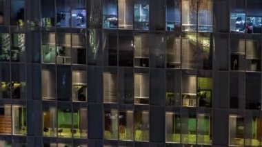 Aydınlatılmış çalışma odaları zaman ayarlı cam panoramik pencere cephesinin gece hava görüntüsü. Gökdelende parlayan ışık