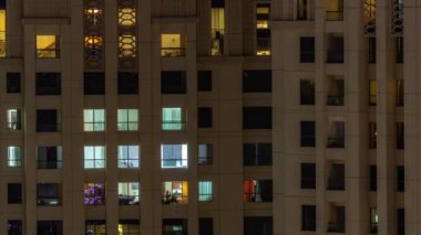 Oturma odalarında parlayan pencereleri olan bir apartman dairesinin akşam manzarası. Işıklı gökdelenle aydınlatılmış yüksek bir gökdelen