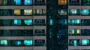 Windows glowing of the multi-storey building of glass and steel lighting and people within timelapse close up view. Dubai, UAE
