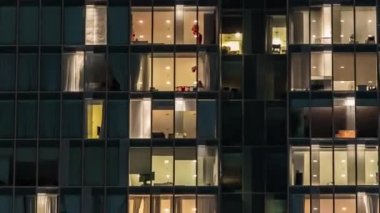 Cam ve çelik ışıklandırmadan oluşan çok katlı binanın penceresinde yanıp sönen ışık ve zaman ayarlı yakın görüş alanındaki insanlar. Dubai, BAE