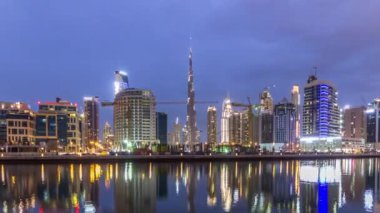 Dubai iş hangarı kuleleri günden geceye geçiş panoramik zaman döngüsü. Aydınlatılmış gökdelenler ve inşaat halindeki yeni kulelerin manzarası. Kanal suyundaki yansımalar.