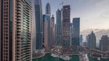Dubai Marina 'da gün doğumundan önce Dubai, BAE' de yatlarla birlikte gece gündüz en yüksek modern gökdelenlerin hava manzarası. Sabahın erken saatlerinde aydınlık kuleler