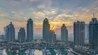 Dubai Marina 'da gündoğumu ışıklarında parlayan modern gökdelenlerin manzarası. Dubai, BAE' de yatları var. Kulelerin arkasında ışık huzmeleri. Gökyüzünde turuncu bulutlar