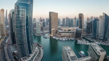 Dubai Marina 'nın gece gündüz aydınlanması. Hava geçiş panoramik zaman dilimi, BAE. Modern gökdelenler ve konut binaları. Yapay kanal şehrindeki alışveriş merkezinin yakınındaki yatlar ve tekneler.