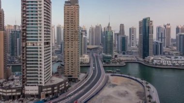 Dubai Marina gezinti güvertesi ve kanalı, gün batımından sonra Dubai, BAE 'de yüzen yatlar ve teknelerle hava üzerinden gece gündüz geçiş zamanı. Modern kuleler ve yol trafiği