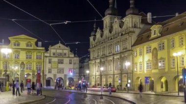 Prag 'da tramvay durağındaki insanlarla aydınlatılmış malostranske namesti meydanının panoramik gece görüntüsü. Aziz Nicolas Kilisesi 'yle ünlüdür. PRAG, ÇEK CUMHURİYETİ
