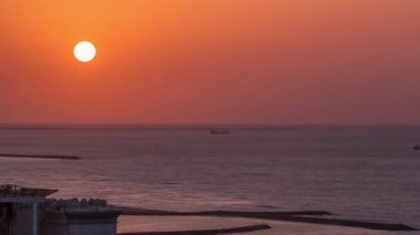 Ajman 'da gün batımı, çatıdaki zaman ayarlı hava manzarası. Birleşik Arap Emirlikleri 'nde turuncu gökyüzünde akşam manzarası. Körfezin kıyı şeridinde su yansımaları var.