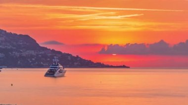 Beaulieu sur mer, Fransa 'dan deniz ve manzaranın gün doğumu görüntüsü. Tekneler ve yatlar ön planda. Güneş bulutların ardından yükseldi. Sudaki yansımalar.