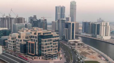 Körfez Meydanı bölgesinden geceye geçiş zamanı. Karışık kullanım ve Dubai 'deki Business Bay' de bulunan düşük katlı kompleks ofis binaları. Yukarıdan hava manzaralı ve yolda trafik var.