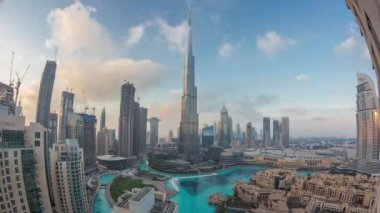 Dubai 'de gökdelenler gün be gece yükseliyor geçiş zamanı, alışveriş merkezi ve çeşme modern binalarla çevrili havadan panoramik manzara bulutlu gün batımı gökyüzü