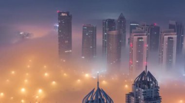 Şeyh Zayed Yolu yakınlarındaki JLT gökdelenleri gece gündüz geçiş zamanı. Aydınlanmış konut binaları ve kavşaktaki trafik. Güneş doğmadan önce sisli bir sabah