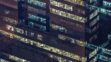 Yüksek katlı ofis binasının pencereleri gecenin geç saatlerinde parlayan ve yanıp sönen iç ışıkları olan dış kısımda. Havadan üst görünüm
