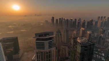Dubai Marina Panoraması 'nda güneş doğarken JLT gökdelenleri ve golf sahası, Dubai, Birleşik Arap Emirlikleri. Yukarıdan hava manzarası sisli bir sabah. Turuncu gökyüzü ile şehir silueti