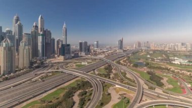 Dubai Marina karayolu kavşağı spagetti kavşağı zaman dilimi. Arka plandaki en uzun gökdelenler ve golf sahası. Gün batımında JLT bölgesinden hava görüntüsü