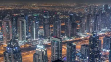 Tüm gece boyunca Sheikh Zayed Yolu yakınlarındaki JLT gökdelenleri ve Dubai marinası. Aydınlatılmış konut binaları ve ışıkları sönük