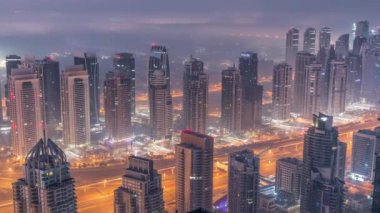 Şeyh Zayed Yolu yakınlarındaki JLT gökdelenleri ve marina kuleleri gece gündüz geçiş zamanı. Aydınlatılmış konut binaları ve villalarla ufuk çizgisi. Güneş doğmadan önce sisli bir sabah