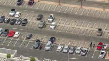 Alışveriş merkezinin yakınındaki büyük otopark birçok araba tarafından dolduruluyor. Araçlar girip çıkıyor.