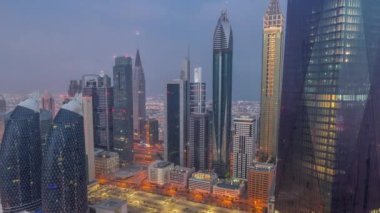 Dubai 'nin finans merkezi, gece gündüz aydınlık lüks gökdelenler geçiş zamanı, Dubai, Birleşik Arap Emirlikleri. Otoparkı ve çatısı olan hava manzarası