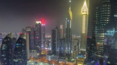 Dubai 'nin finans merkezi, tüm gece boyunca aydınlık lüks gökdelenler, Dubai, Birleşik Arap Emirlikleri. Otoparkı ve çatıları sisle kaplı olan gökyüzü manzarası. Işıklar dönüyor.