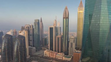 Dubai 'nin finans merkezi lüks gökdelenleri ve büyük park sabahı zaman çizelgesi, Dubai, Birleşik Arap Emirlikleri. Ofis kuleleriyle hava manzarası ve güneş doğarken cam yüzeyden yansımalar