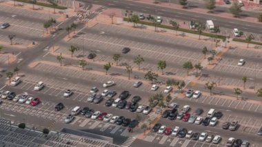 Alışveriş merkezinin yakınındaki büyük otopark birçok araba tarafından dolduruluyor. Bütün gün hareket eden gölgelerle araçlar girip çıkıyor.